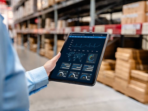 Businessman using digital tablet with warehouse management system dashboard on screen, monitoring inventory, delivery, and supply chain analytics in smart logistics distribution center